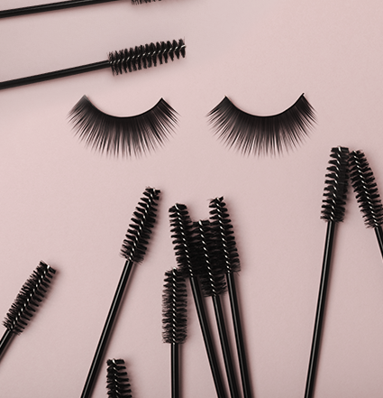 Două gene în centru, înconjurate de baghete de rimel pe un fundal roz